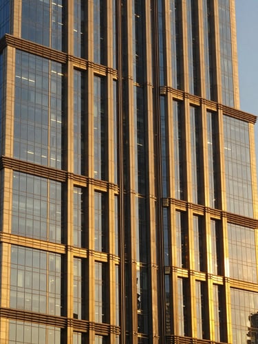 Close-up architectural photography of a modern Dubai skyscraper facade, sharp geometric brass and glass details, warm golden-hour light