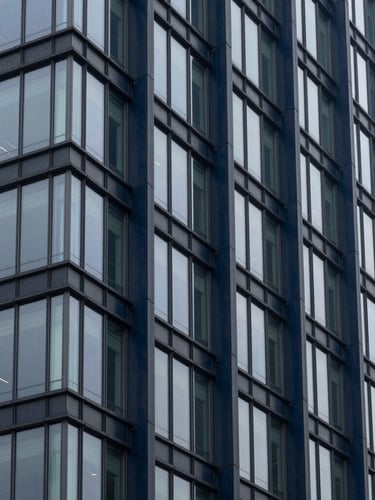Architectural detail of a modern financial district building with structural glass and deep navy steel columns, cool overcast daylight.