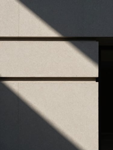 Architectural detail of a minimalist venue facade, harsh direct sunlight casting sharp diagonal shadows.