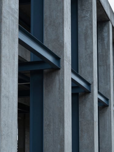 Low-angle architectural perspective of structural steel and concrete pillars, sharp shadows, cool overcast daylight, deep slate tones