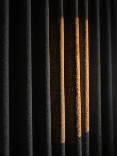Dramatic close-up of heavy charcoal linen curtains catching low-angle golden side light, deep shadows, moody editorial interior photography, 35mm lens