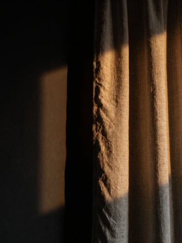 Dramatic close-up of heavy linen curtain catching low-angle side light, casting deep shadows on a matte black wall, moody editorial interior photography, 35mm lens