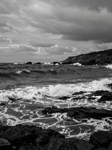 Dramatic black and white photograph of the rugged Ordu coastline, dark moody sea with crashing waves, overcast coastal daylight, high contrast, fine art photography style