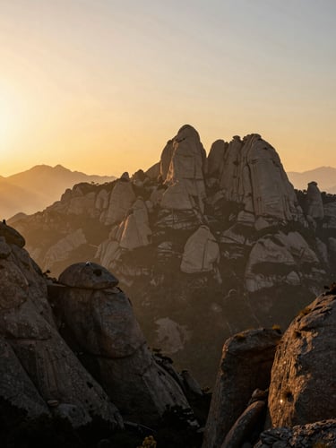 Wide panoramic view of the Montserrat mountain range at sunrise, rugged peaks silhouetted against a golden sky, atmospheric mist in the valleys