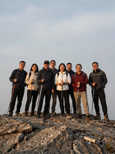 A group of cheerful hikers standing together at a mountain summit, holding walking poles, smiling under a soft overcast sky, rugged stone ground