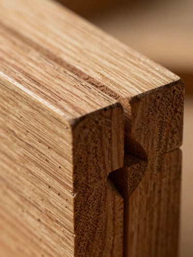 Macro detail shot of an interlocking mortise and tenon wood joint, warm tactile photography, natural workshop side-lighting, rich organic oak texture, shallow depth of field