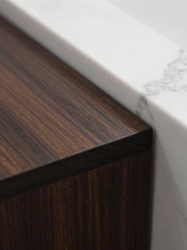 Macro close-up of a dust-free, gleaming dark wood surface meeting a clean white marble countertop, sharp natural light casting soft shadows.