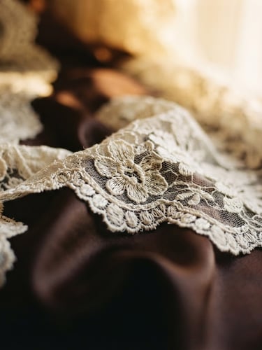 Extreme close-up of delicate cream lace draped over deep espresso satin, warm golden-hour window light, shallow depth of field, 35mm film