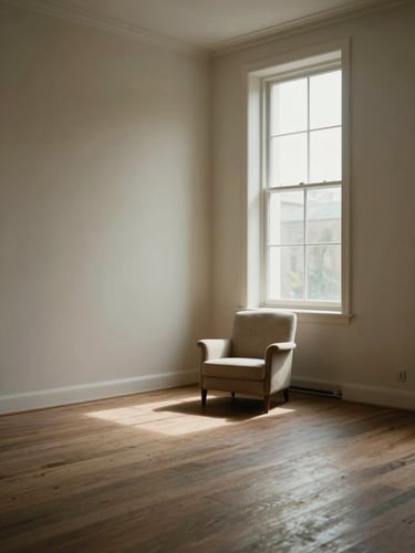 An empty room with light wood floors and a single beige armchair next to a large sunlit window, highlighting minimalist