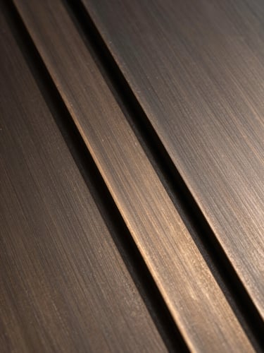 Portrait detail of dark brushed bronze metal plates overlapping with a sharp geometric shadow, warm natural light