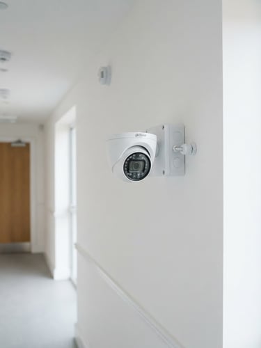 Foto instalasi kamera CCTV terpasang rapi di dinding bersih, kabel tersembunyi, dengan pencahayaan alami terang, fokus tajam.
