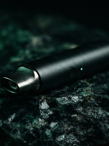 Macro photograph of a sleek matte-black vaporizer resting on a dark obsidian stone surface, emerald green ambient glow, dramatic low-key side-lighting, shallow depth of field
