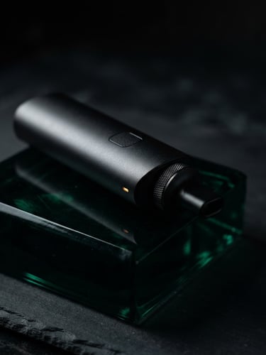 Close-up of a sleek matte-black vaporizer resting on a dark emerald glass block, dramatic side-lighting, macro lens, shallow depth of field