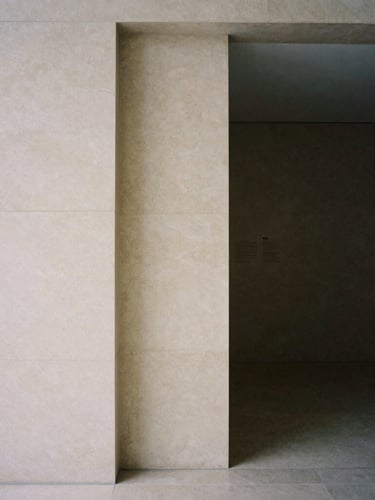 A minimalist architectural detail of a private gallery entrance, soft indirect natural light, deep quiet shadows, warm alabaster stone, medium format film