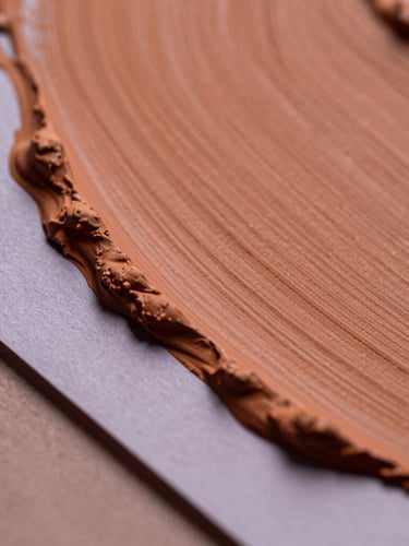 Macro close-up of textured terracotta paint strokes overlapping soft lavender paper layers, cast in soft side-lighting with subtle shadows, tactile editorial photography.