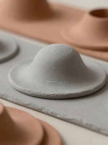 A close-up of layered clay models in soft ash gray and terracotta tones, casting subtle shadows under diffused natural studio light.
