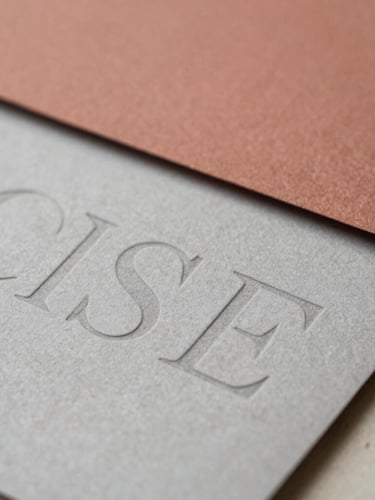 Close-up of physical brand collateral with layered paper textures and debossed typography under soft natural light