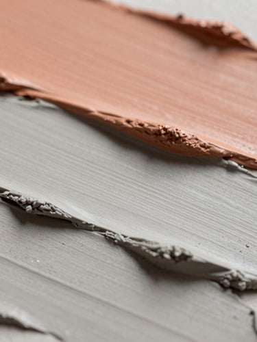 Macro photograph of layered ash gray clay and soft terracotta paint strokes, soft side-lighting casting delicate shadows, tactile editorial style.