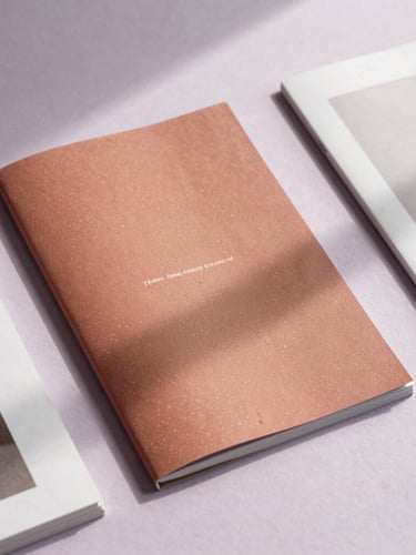 Staggered flat-lay of printed editorial lookbooks on a mist lavender background, soft natural daylight casting delicate shadows.