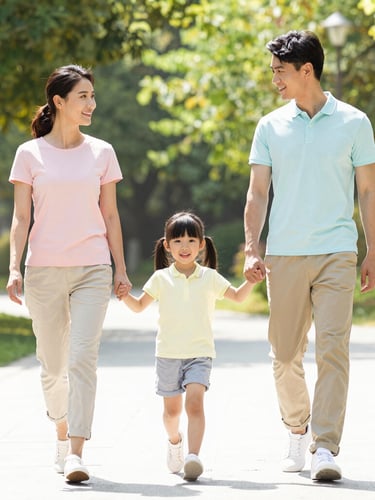 Bright high-key lifestyle photography of a smiling mother, father, and young daughter in coordinated pastel casual wear walking together in a sunlit park, natural daylight, crisp focus, 35mm lens