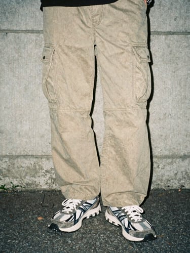 Casual eye-level snapshot of Tokyo street style, a person wearing oversized cargo pants and vintage sneakers, natural flash-lit lighting on a concrete background, 35mm film grain.