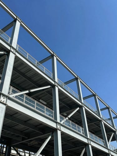 Low-angle architectural shot of a massive steel structure against a bright blue sky, sharp industrial lines, high-contrast