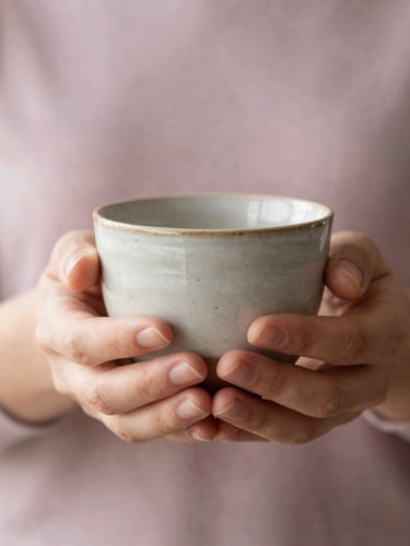 A close-up of gentle hands holding a warm, textured ceramic cup, soft diffused morning light, shallow depth of field, peaceful and elegant.