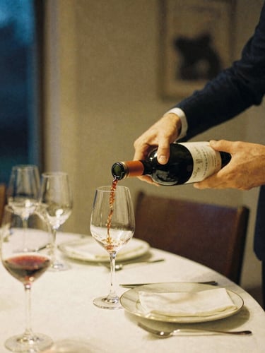Warm editorial 35mm photography, soft evening ambient light, medium shot of a host pouring wine into elegant glasses at a home dining table, rich navy and gold tones.
