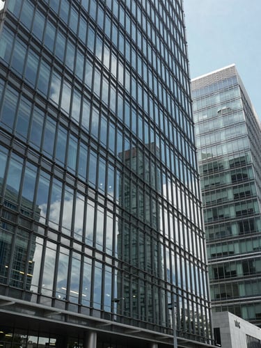 Wide panoramic view of modern glass office architecture in Malabo II, sharp geometric lines, clean reflections under crisp daylight, high-contrast corporate framing.