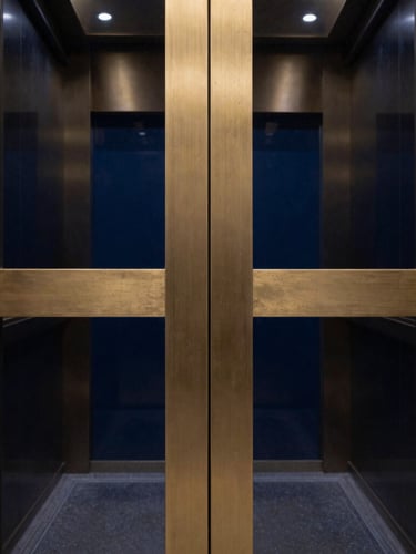 Extreme macro photograph of restored architectural bronze elevator doors, flawless grain, high-contrast dramatic lighting, deep navy reflections, gold metallic sheen, 35mm.