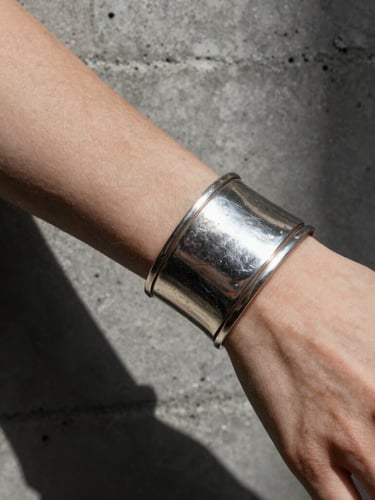Extreme close-up of a heavily patinated silver cuff on a woman's wrist against a raw concrete wall, stark studio lighting, deep shadows.