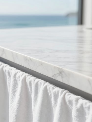 Extreme close-up of an immaculate white marble countertop with sharp reflections, bright natural coastal daylight, minimalist composition, 35mm.
