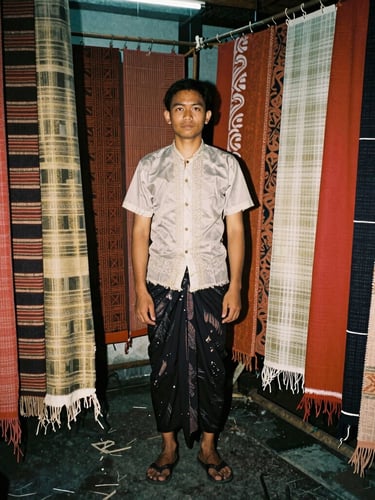 Tight 35mm flash portrait of a local Balinese designer in a humid studio, surrounded by distressed deadstock textiles, raw analog warmth, direct flash shadows.