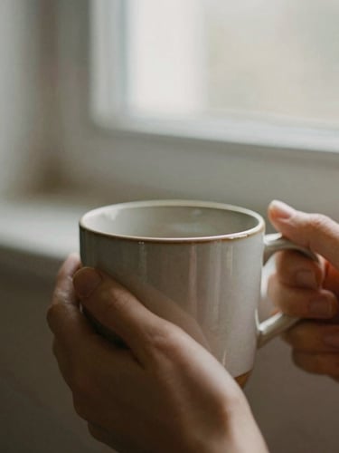 Intimate close-up of hands holding a warm ceramic mug in soft morning window light, low contrast, muted earthy tones, shallow depth of field, 35mm film grain
