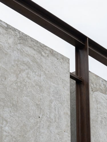 Close-up of architectural materials, raw concrete texture and dark steel frame under natural overcast daylight, sharp focus, minimalist composition.