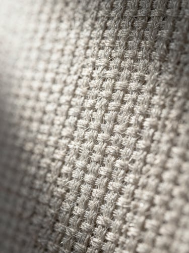 Extreme macro close-up of a dense technical textile weave, raking cool studio strobe light from upper left revealing individual thread interlacing and fiber texture, neutral off-white and slate grey tones, sharp focus edge-to-edge, no depth-of-field blur