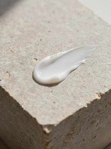 Minimalist composition of a single cosmetic cream swatch on a textured limestone block, soft diffused daylight, gentle shadows, macro lens, editorial style.