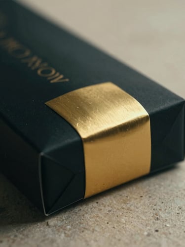 Macro close-up of premium minimalist black and gold product packaging on a clean stone surface, soft dramatic side lighting, shallow depth of field.