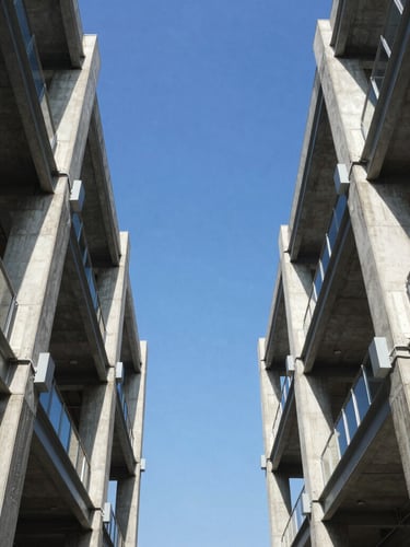 Symmetrical low-angle architectural shot of a modern steel and concrete commercial structure framing a bright blue sky, high contrast daylight