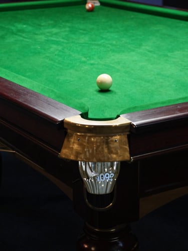 Moody editorial photography of a pristine snooker table corner, polished brass pocket, deep forest green felt under dramatic overhead spotlight, 35mm