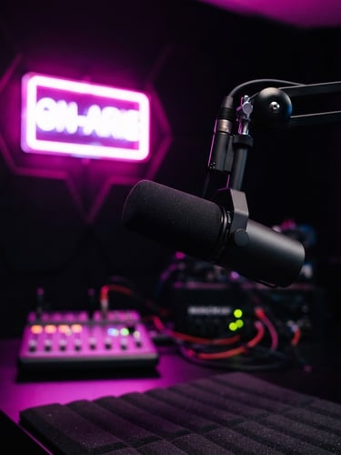Close-up of a modern professional broadcasting microphone in a dark radio studio, glowing fuchsia and violet on-air light in the background, vibrant digital photography, high-contrast neon lighting