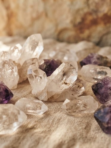 A collection of natural clear quartz and purple amethyst crystal clusters resting on a linen fabric.