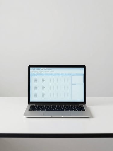 Straight-on medium shot of a minimalist office desk in bright neutral daylight, a modern laptop showing a clean spreadsheet, soft corporate blue tones, sharp focus, 35mm