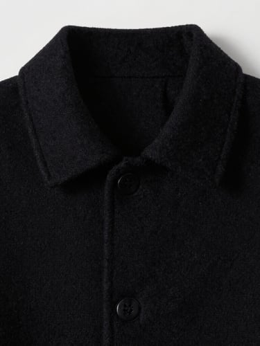 Detail shot of structural seams on a heavy black wool collar, sharp directional studio lighting, high contrast, desaturated cool tones