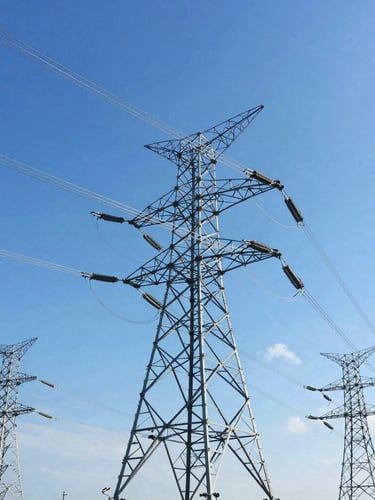 Low-angle environmental shot of modern high-voltage transmission towers stretching into a bright blue sky, crisp daylight, high-contrast industrial photography