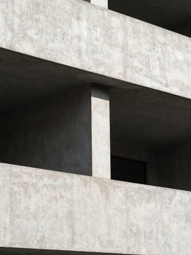 A high-contrast, minimalist architectural photograph of a concrete building facade under bright daylight, clean geometric lines and deep shadows creating structured negative space.