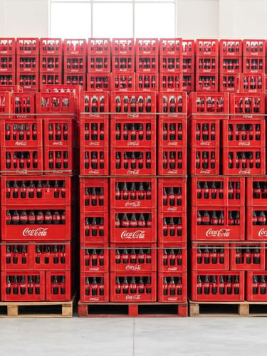 Straight-on medium shot of stacked red Coca-Cola crates in a brightly lit, clean Gopalganj warehouse, vibrant red tones, high-key commercial lighting, 35mm
