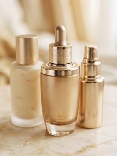 Pristine unopened luxury cosmetic bottles in warm champagne gold tones, soft diffused daylight, macro product details, 35mm