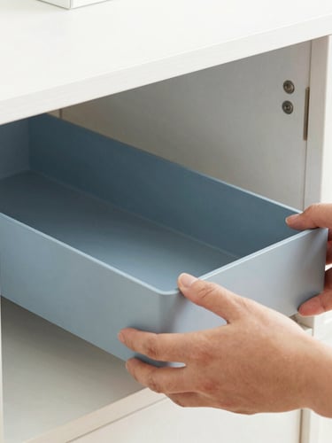 Close-up of hands placing a sleek, unbranded modular drawer organizer inside a clean white wooden cabinet, bright natural lighting