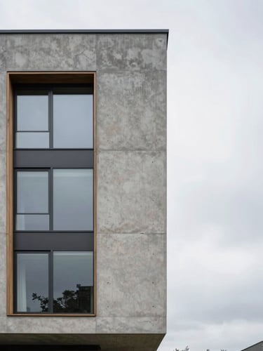 Sharp, straight-on architectural elevation of a modern concrete and glass residence facade, overcast daylight emphasizing raw textures of slate and wood, minimalist composition with generous negative space on the right.
